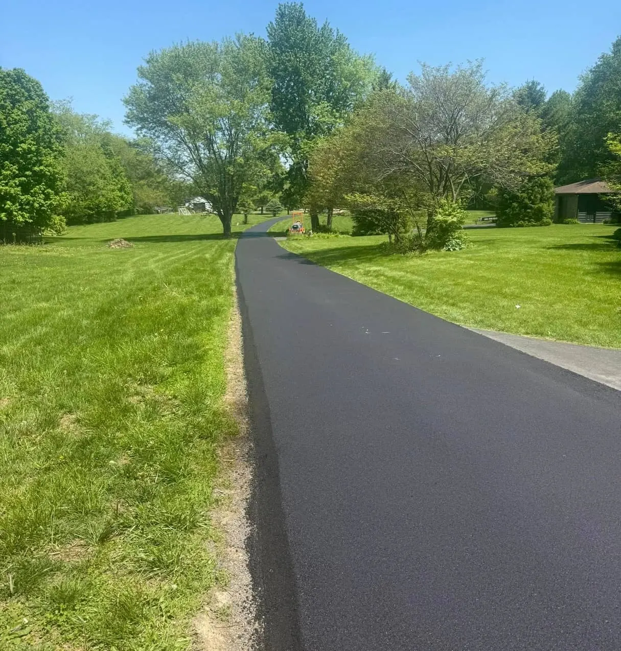 Freshly paved asphalt private road stretching through a lush green lawn and mature trees